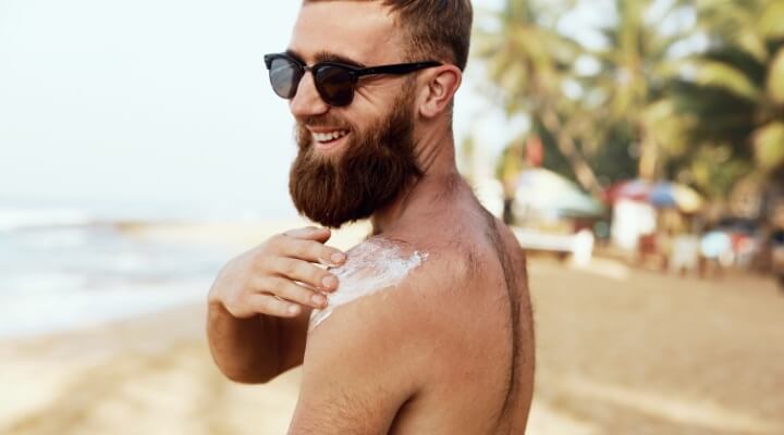 man putting sunscreen on at beach